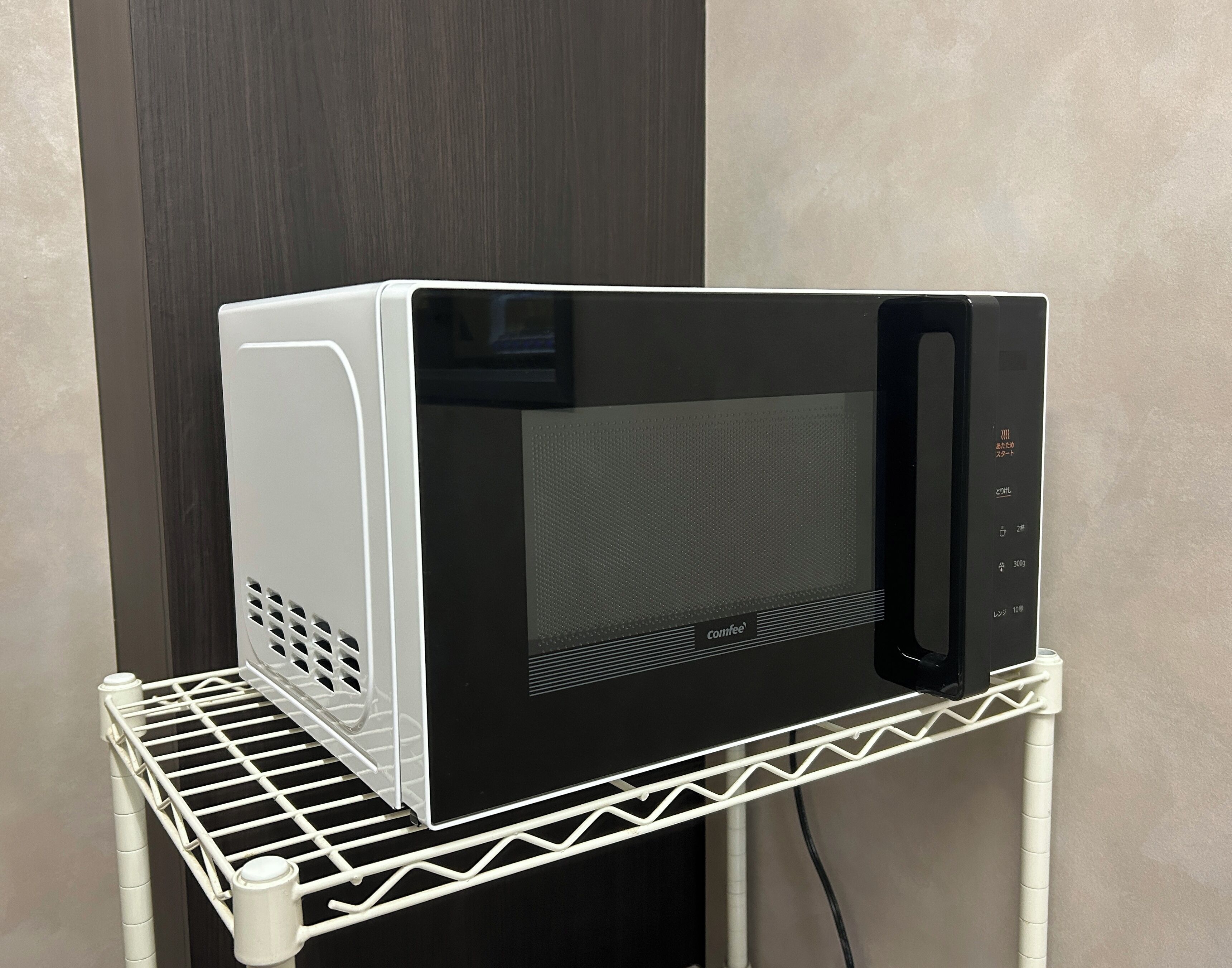 Un four à micro-ondes posé sur une étagère en métal blanc.