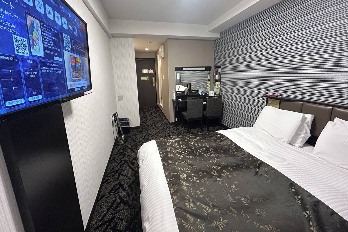 A hotel room with a bed, a desk, and a television displaying information.