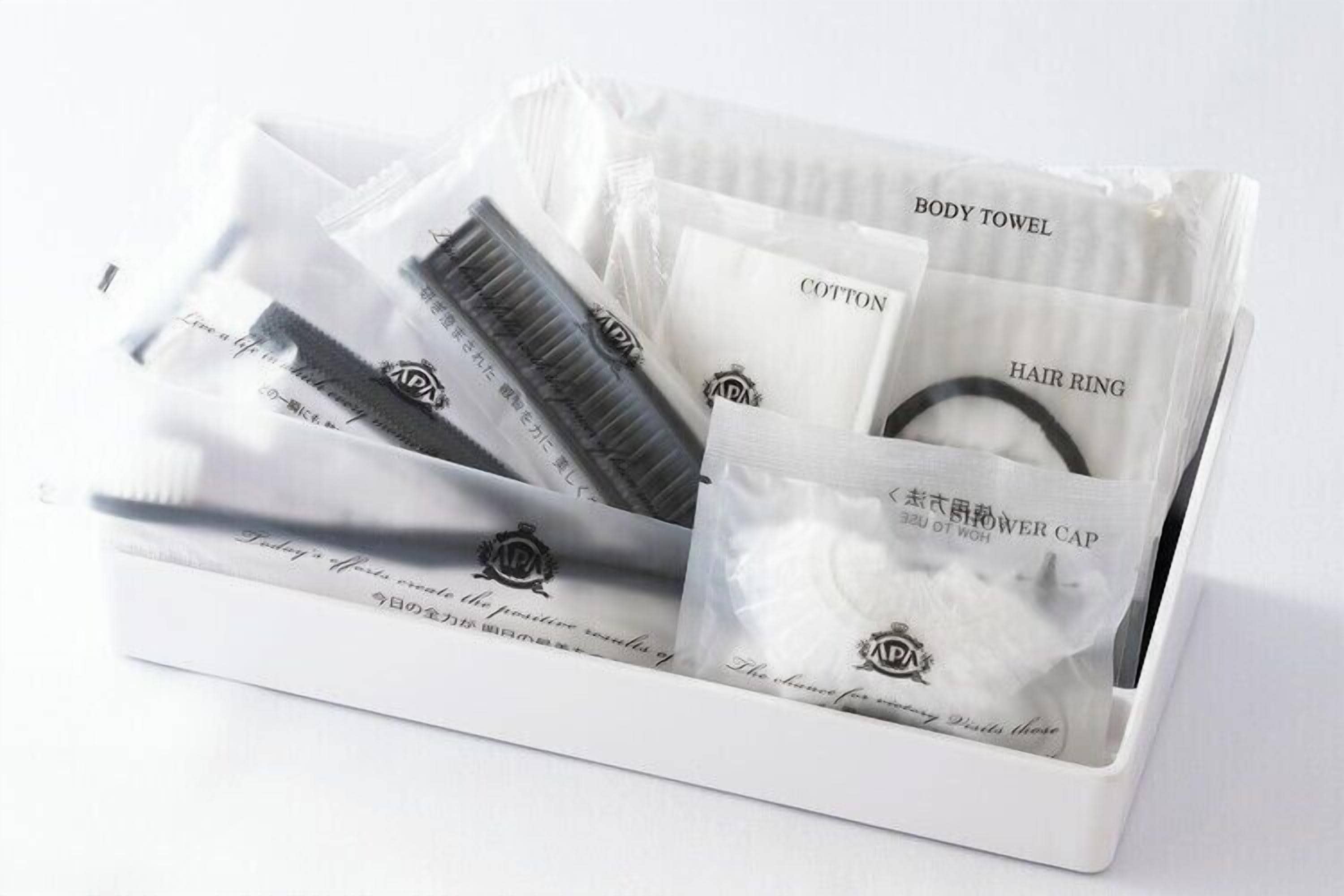 A white box containing a body towel, cotton, a hair ring, and a shower cap.
