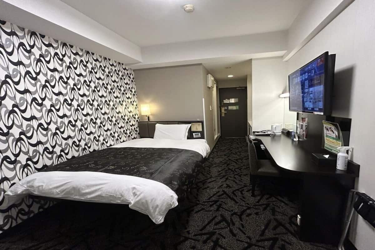 A hotel room with a bed, a desk, a television, and a patterned wall.