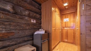 Interior de una cabaña de troncos con pared de madera, un refrigerador, un banco de madera y una puerta con un cartel.