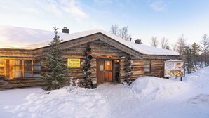 Una cabaña de madera con puerta de madera, techo cubierto de nieve y un cartel.