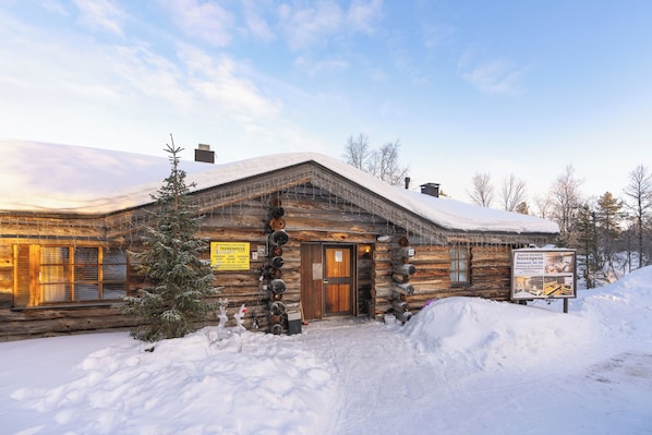 A log cabin with a wooden door, a snow-covered roof, and a signboard.