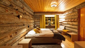 Un dormitorio de cabaña de madera con una cama, mesitas de noche, una silla y una ventana con cortinas.