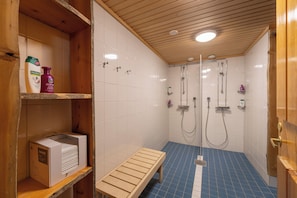 A shower area with two glass-enclosed showerheads, a bench, and shelves with toiletries.