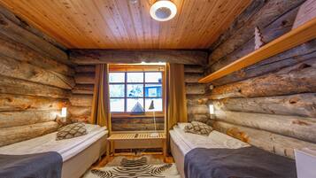 A log cabin room with two beds, a zebra-patterned rug, a window with curtains, and a wooden ceiling.