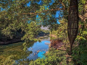 A serene riverside view with a wooden bridge and dense foliage.