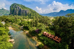 Une rivière traverse une vallée verdoyante, avec une montagne imposante en arrière-plan et des bâtiments de style traditionnel le long de ses rives.