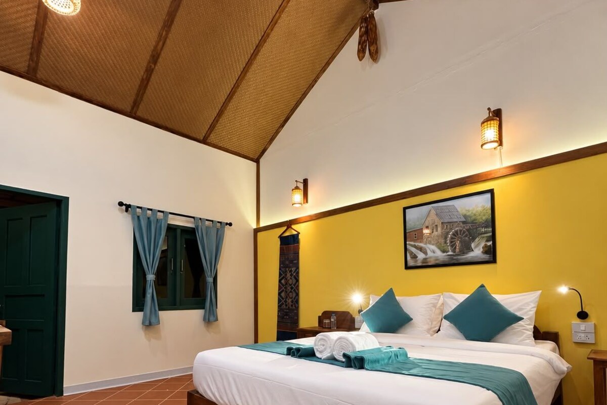 Une chambre d’hôtel avec un grand lit, un plafond en bois et un mur jaune.