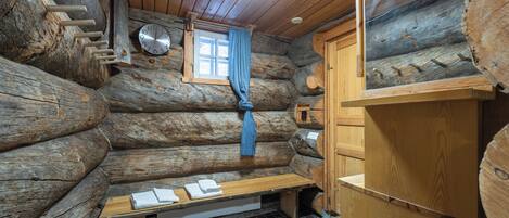 A log cabin interior with a wooden bench, a small window with a curtain, and a wooden cabinet.