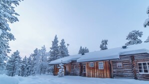 A log cabin with a snow-covered roof, surrounded by snow-laden trees. - Kuukkeli Apartments Tokka (Saariselka)