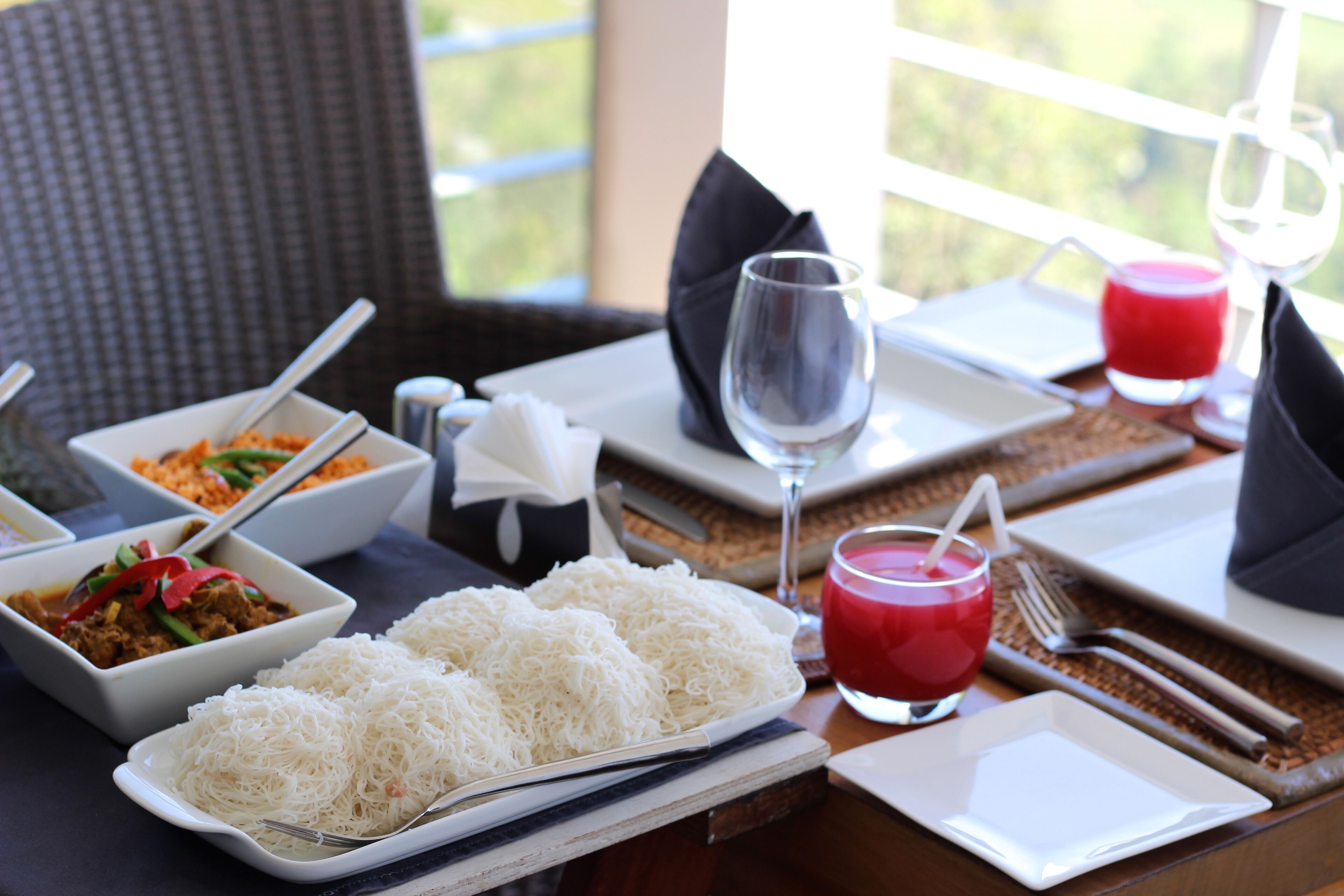 A dining table set with white plates, bowls of food, a glass of red drink, and cutlery.