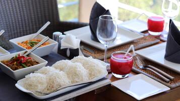 A dining table set with white plates, bowls of food, a glass of red drink, and cutlery.
