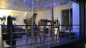 Una sala de estar moderna con un separador de vidrio, un techo con luces de cuerda y diferentes opciones de asiento, incluyendo un sofá y sillones.