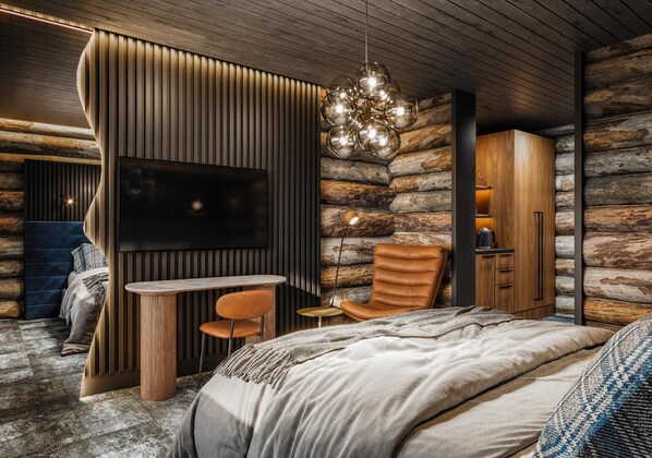 A log cabin interior with a bed, a TV, a dining table, and a leather chair. - Kuukkeli Log Houses Porakka Inn (Saariselka)