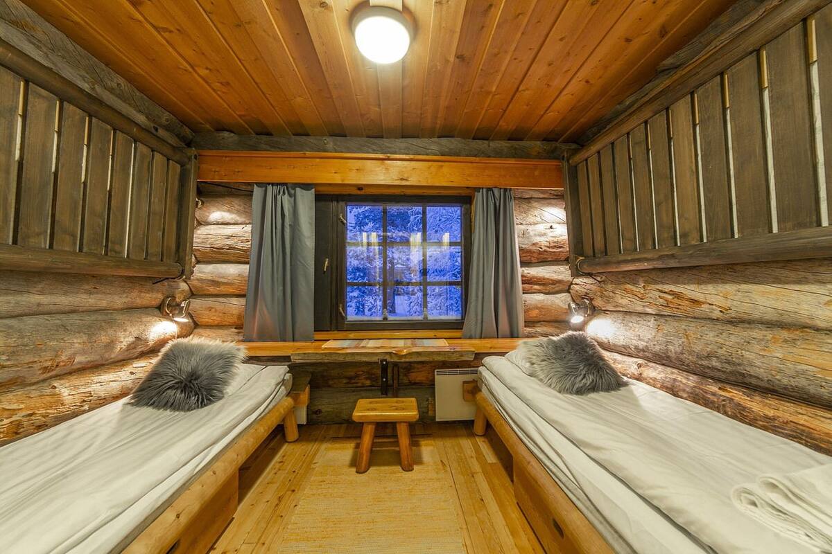 A log cabin room with two beds, a small table, and a window with curtains.