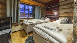 Un dormitorio rústico de madera con dos camas, techo de madera y ventana con vista a un paisaje nevado.