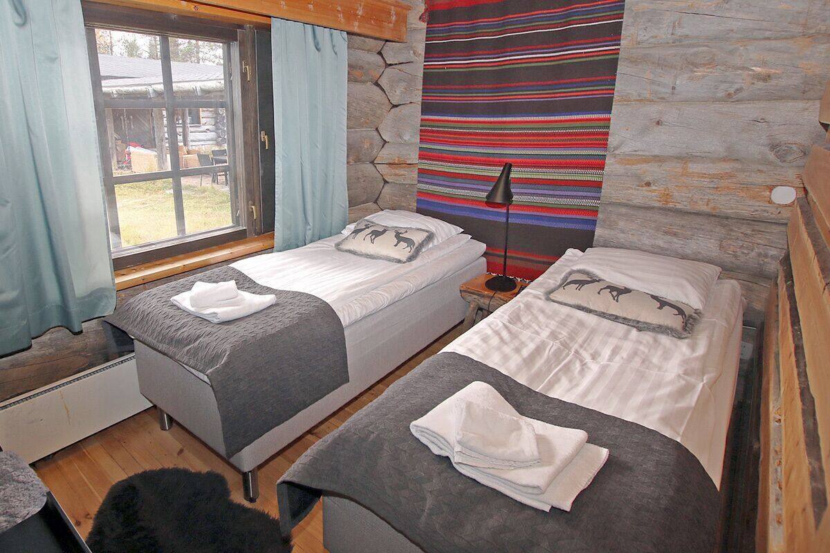 A room with two beds, a window, a stone wall, and a colorful tapestry.