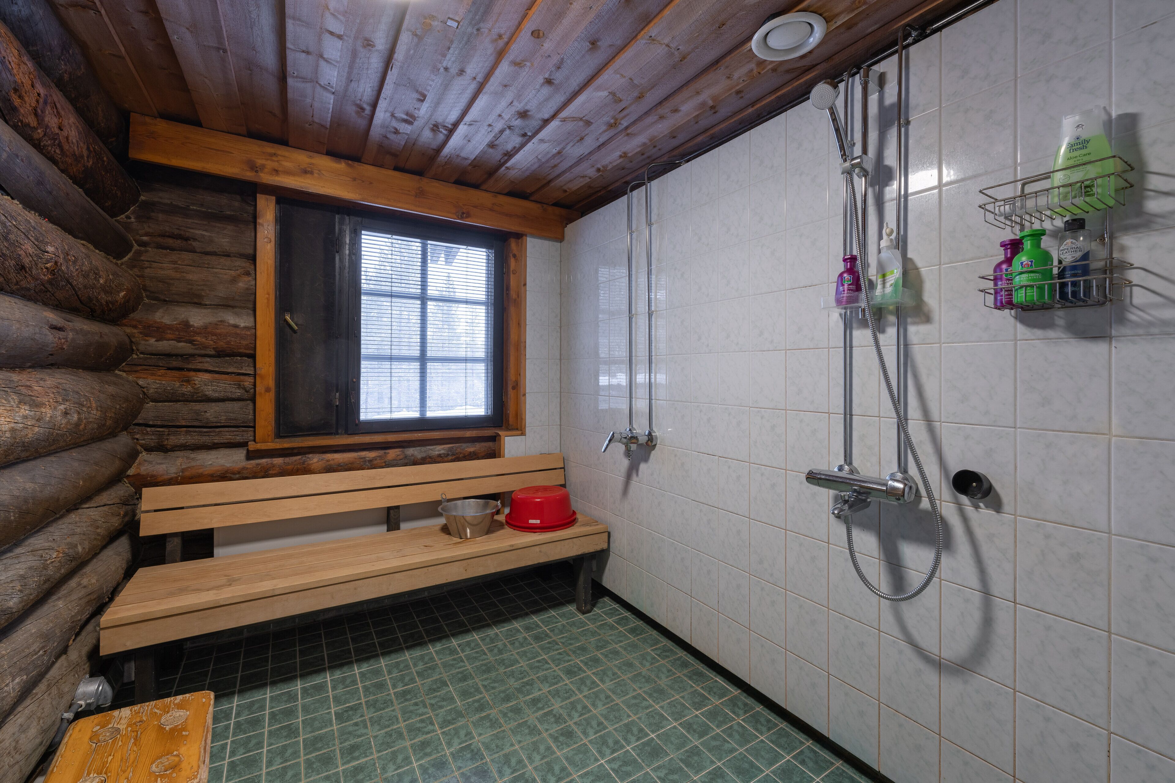 Un baño de cabaña de troncos con un banco de madera, un ventanal, ducha y paredes de azulejos.