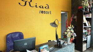 A reception desk at Riad Resort with a computer, a desk lamp, and a vase of flowers. - Riad Resort (Aranyaprathet)