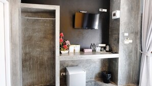 A compact room with a mounted TV, a small fridge, a shelf with toiletries, and a door leading to another space. - Riad Resort (Aranyaprathet)