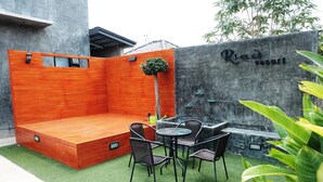 A modern outdoor seating area with a wooden bench, a small table, and chairs, surrounded by green artificial turf and a concrete wall with a sign reading "Road Resort". - Riad Resort (Aranyaprathet)