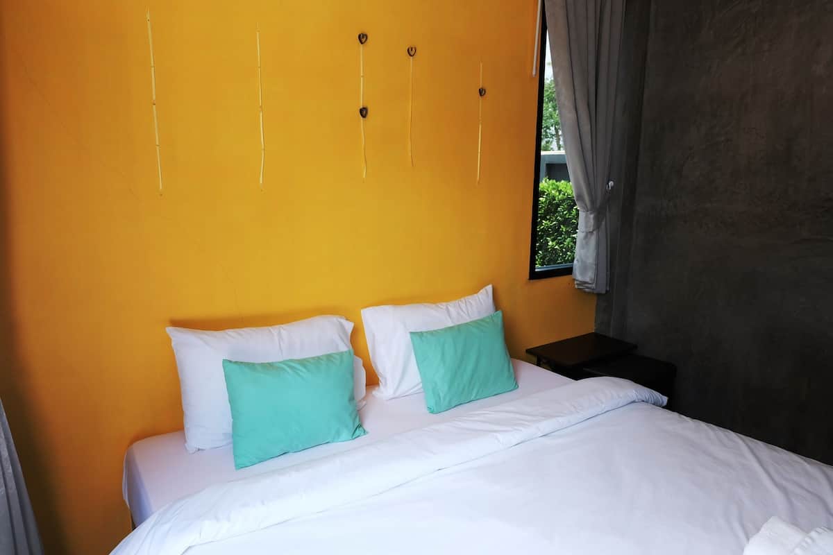 A hotel room with a bed, two pillows, a nightstand, and a window with curtains.