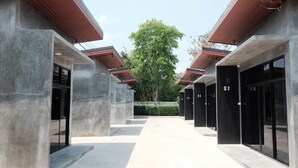 A modern building with a central open space, concrete pillars, and black doors numbered 82 and 83. - Riad Resort (Aranyaprathet)
