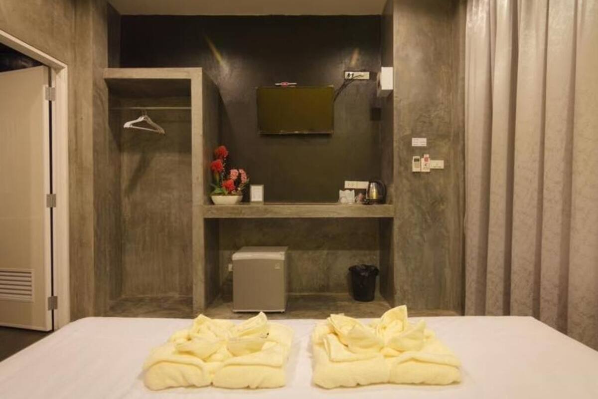 A hotel room with a bed, a small seating area with a chair and a table, a mirror, and a television mounted on the wall.