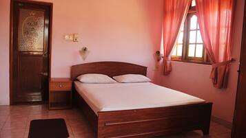 A bedroom with a wooden bed, a nightstand, a door with a decorative glass panel, and a window with curtains.