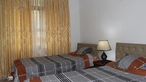 Una habitación de hotel con dos camas, una mesita de noche con lámpara y una ventana con cortinas.