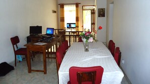 Un comedor con una mesa larga, sillas rojas, una computadora portátil y un florero con flores.
