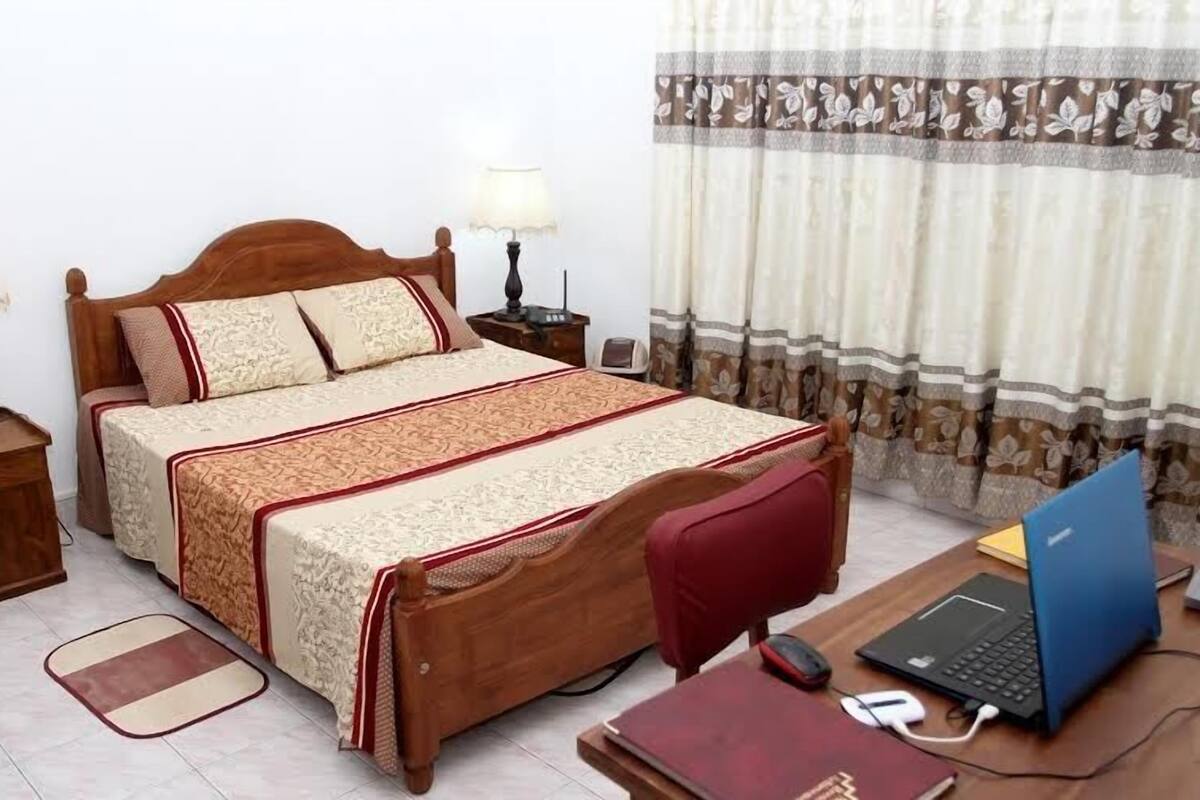 A bedroom with a wooden bed, two bedside tables with lamps, a desk with a laptop, and a chair.