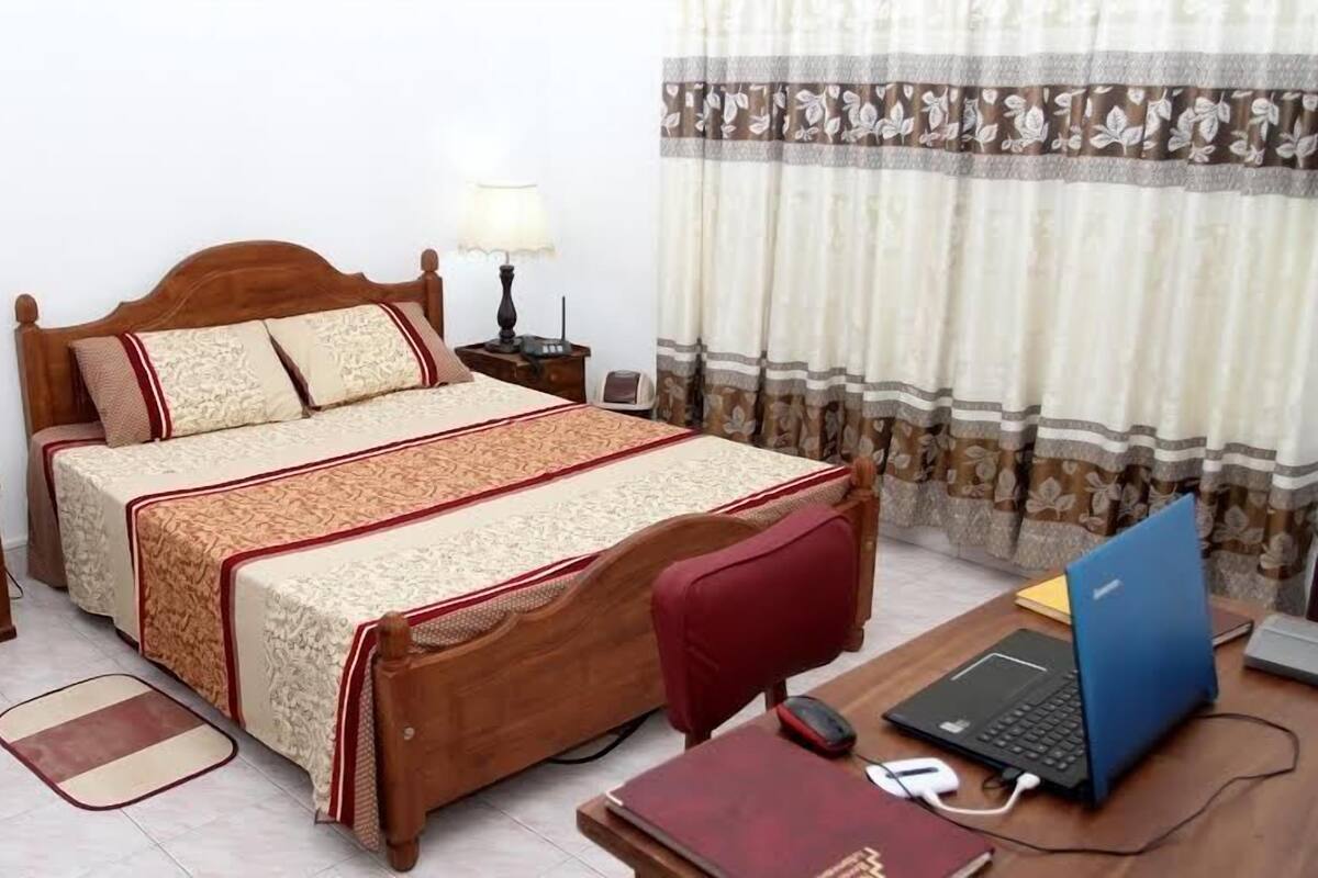 A bedroom with a wooden bed, two bedside lamps, a desk with a laptop, and a chair.