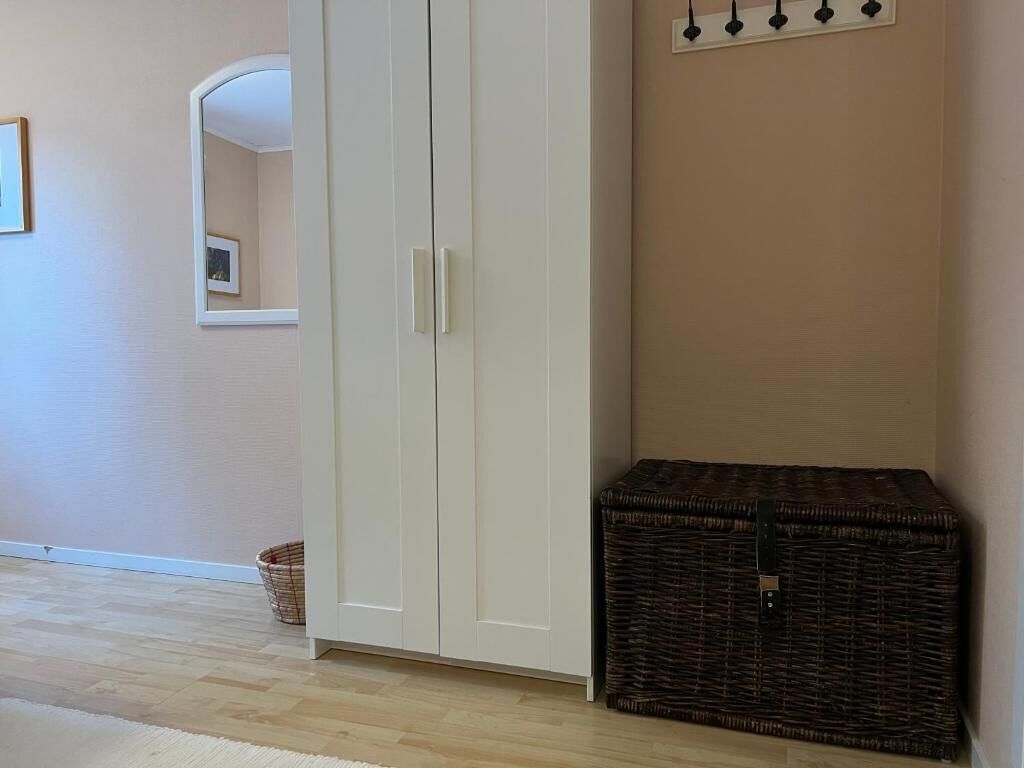 A room with a wardrobe, a wicker chest, and a wall-mounted coat hook.