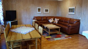 Un soggiorno con parete in legno, un divano in pelle marrone, un tavolo da pranzo in legno con sedie, un televisore e tre quadri incorniciati.