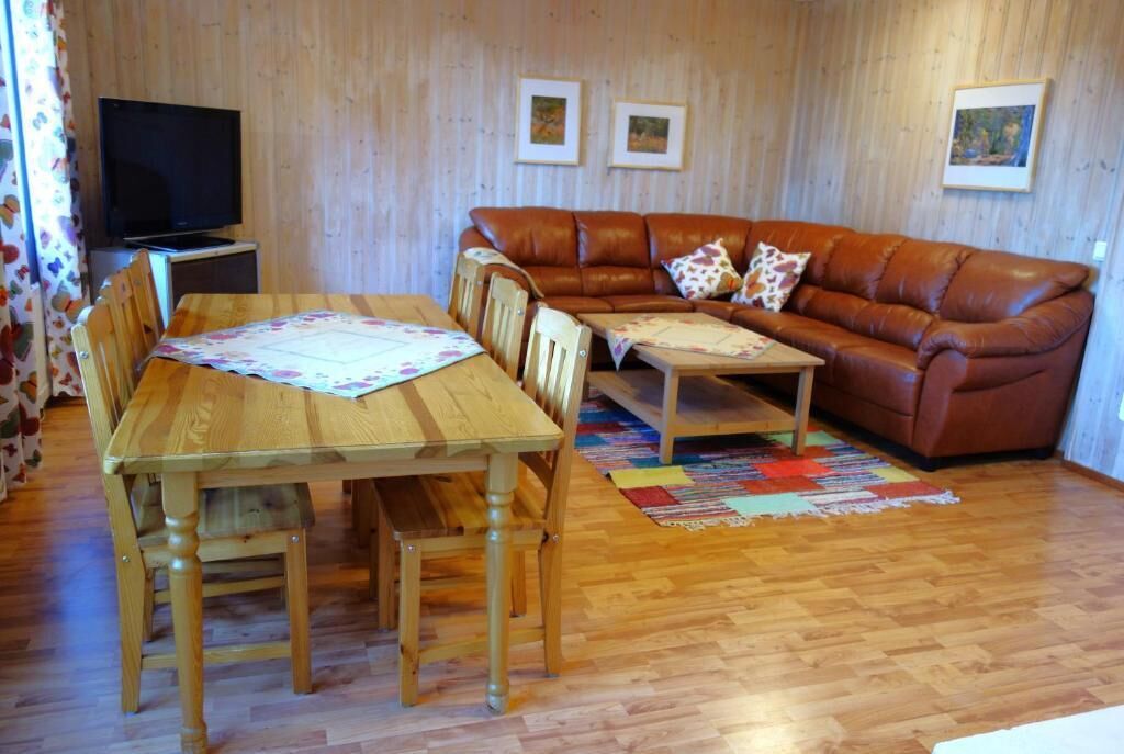 Una mesa de comedor de madera, sillas, un sofá de cuero marrón y un televisor sobre un mueble bajo.