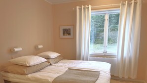 Una camera da letto con un letto, una sedia, una finestra con tende, un termosifone e un quadro appeso al muro.