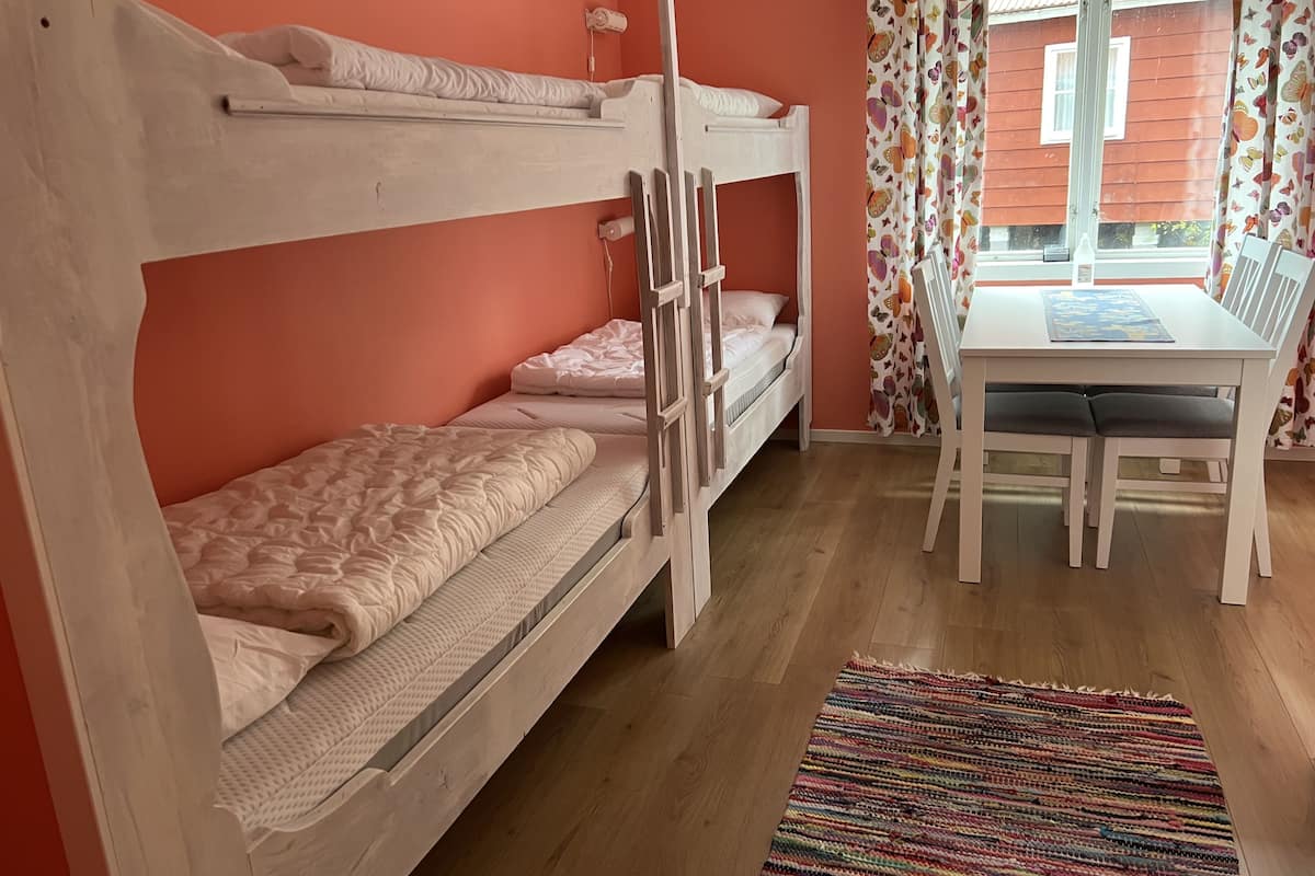 Een kamer met stapelbedden, een tafel en een kleurrijk vloerkleed.