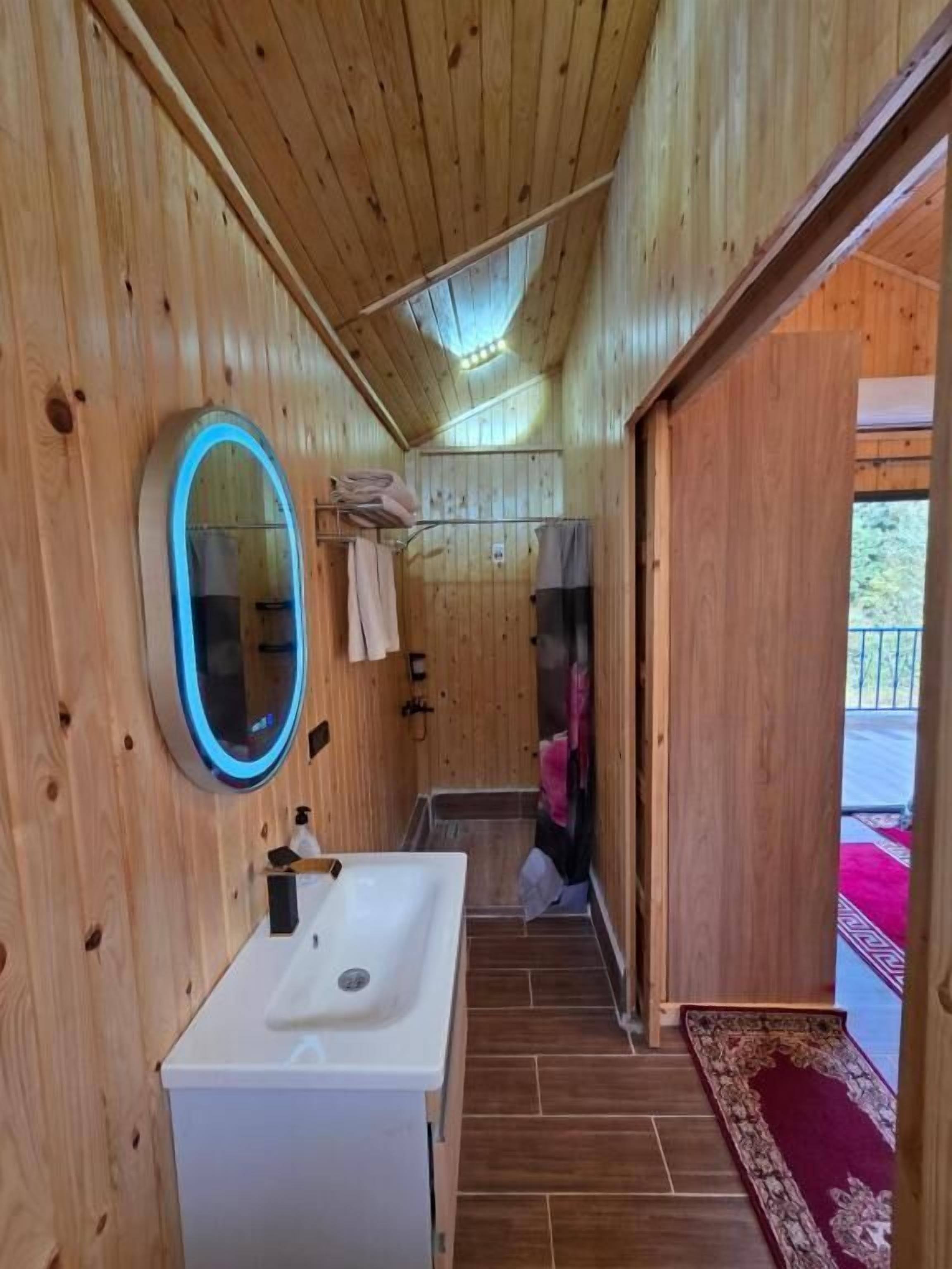 A wooden cabin bathroom with a white sink, a mirror, and a shower area.