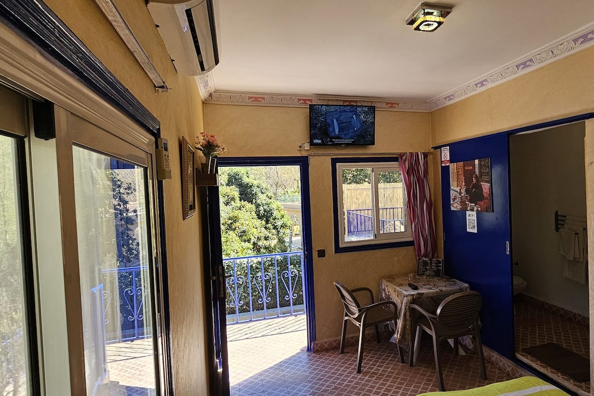A hotel room with a balcony, a television, a small table with chairs, and a sign on the wall.