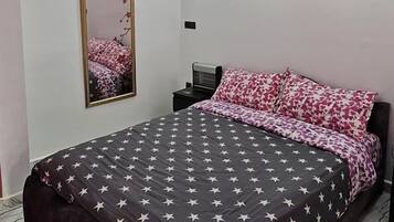 A bedroom with a bed, a mirror, a window with flower paintings, and an air conditioning unit.