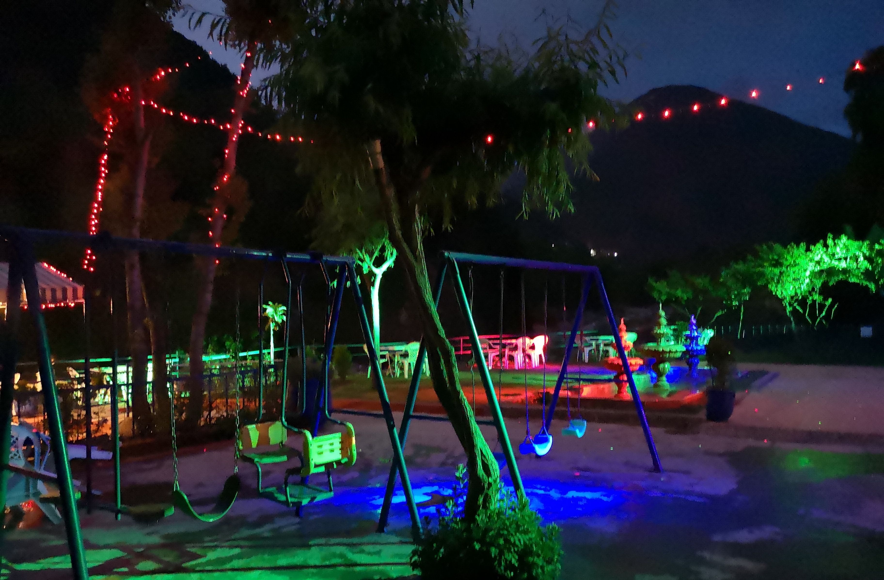 Un espace extérieur aménagé pour les soirées, avec des balançoires et une fontaine, le tout illuminé de lumières colorées.