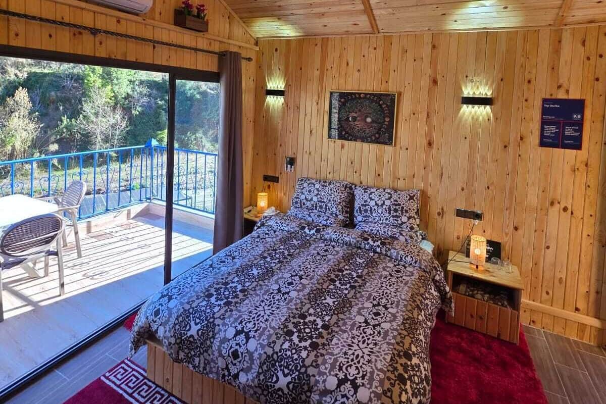 A wooden-paneled bedroom with a bed, bedside tables, and a view to an outdoor deck.