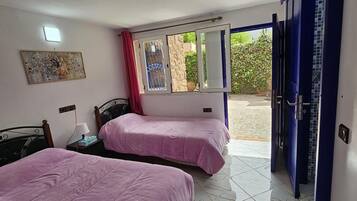 Un dormitorio con dos camas, una ventana con vista a follaje y una puerta que da al exterior.