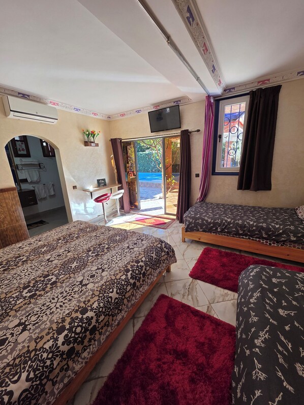Habitación de hotel con dos camas, un televisor, una mesita y un baño visible a través de un arco.