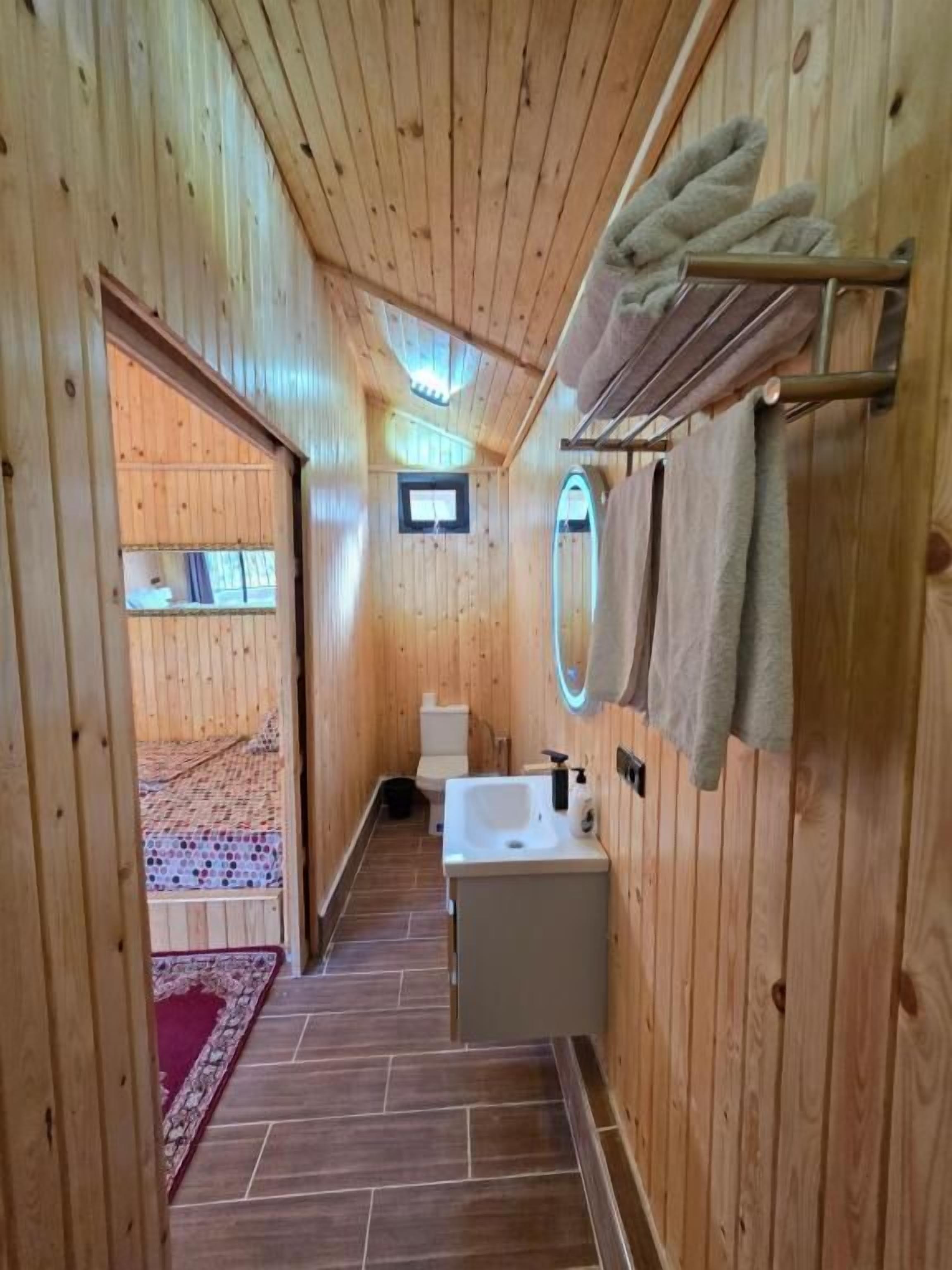 Une salle de bain aux murs lambrés, équipée d’un lavabo, de toilettes et d’un miroir.