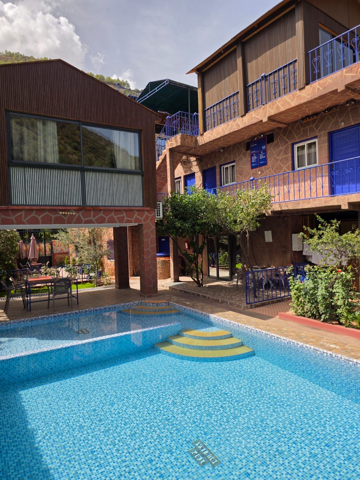 A hotel with a swimming pool, outdoor seating, and a mountainous backdrop.