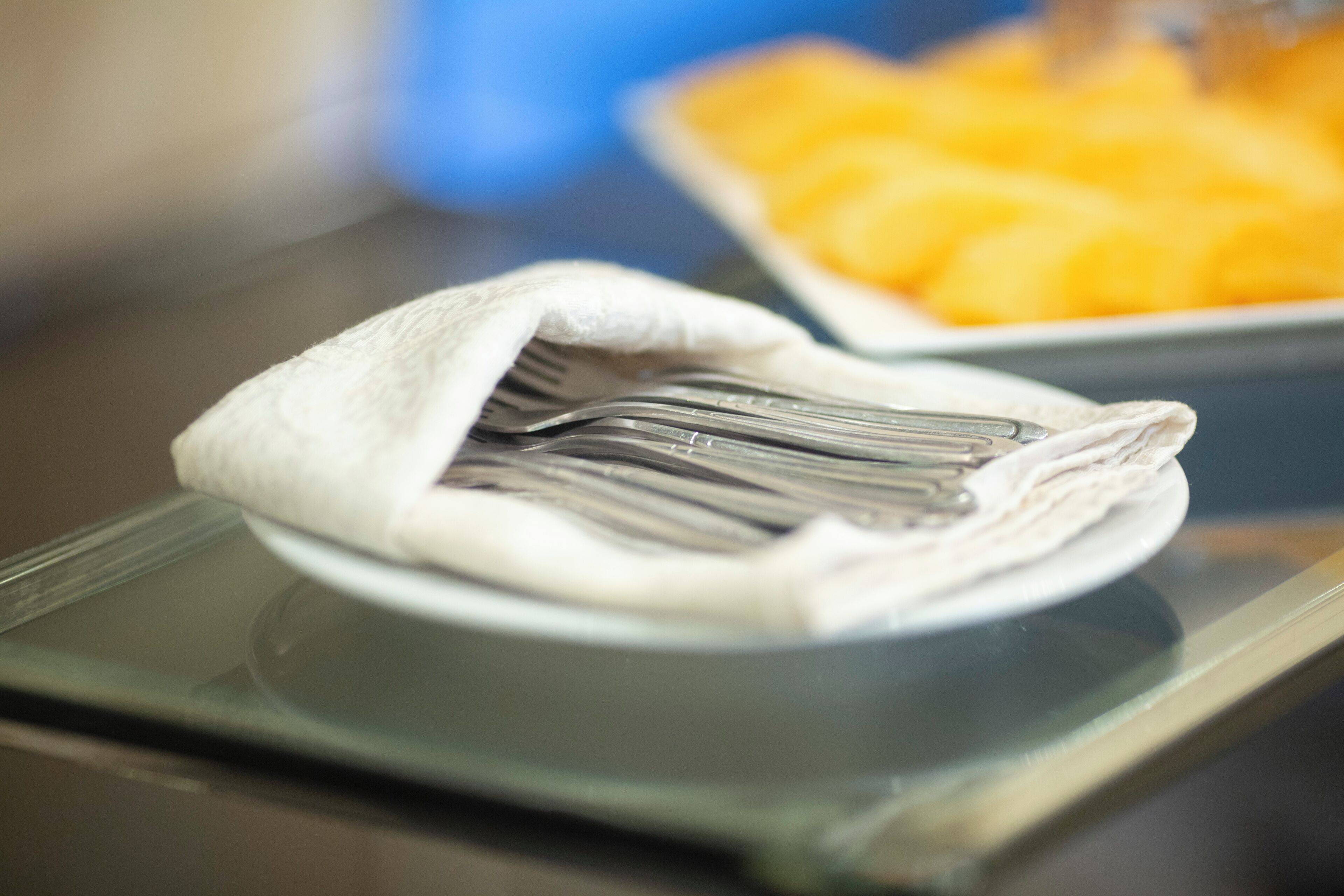 A plate with folded napkins and cutlery on a glass table.