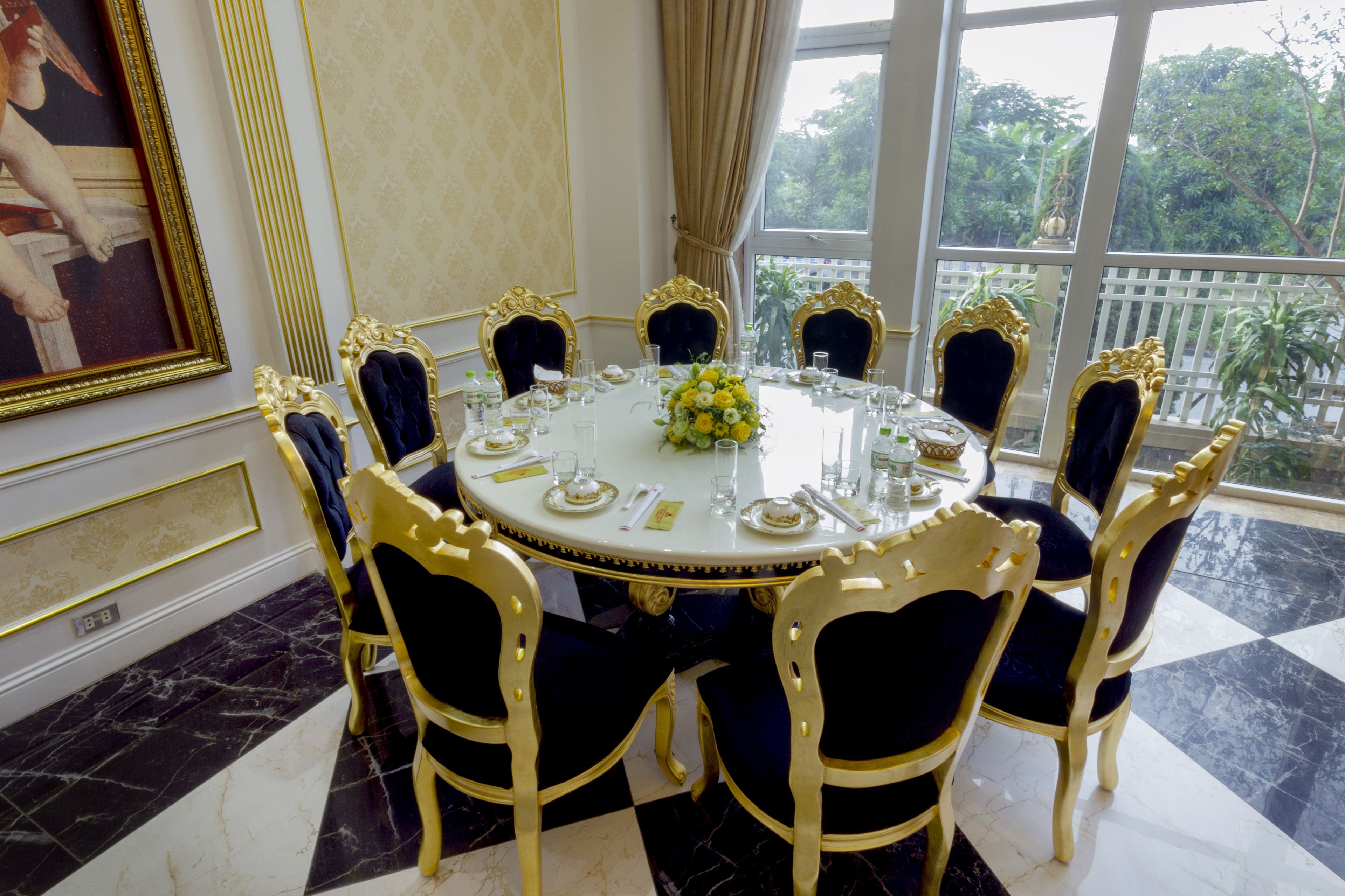 Una mesa de comedor redonda con sillas de detalles dorados, un mantel blanco y un centro de mesa floral.